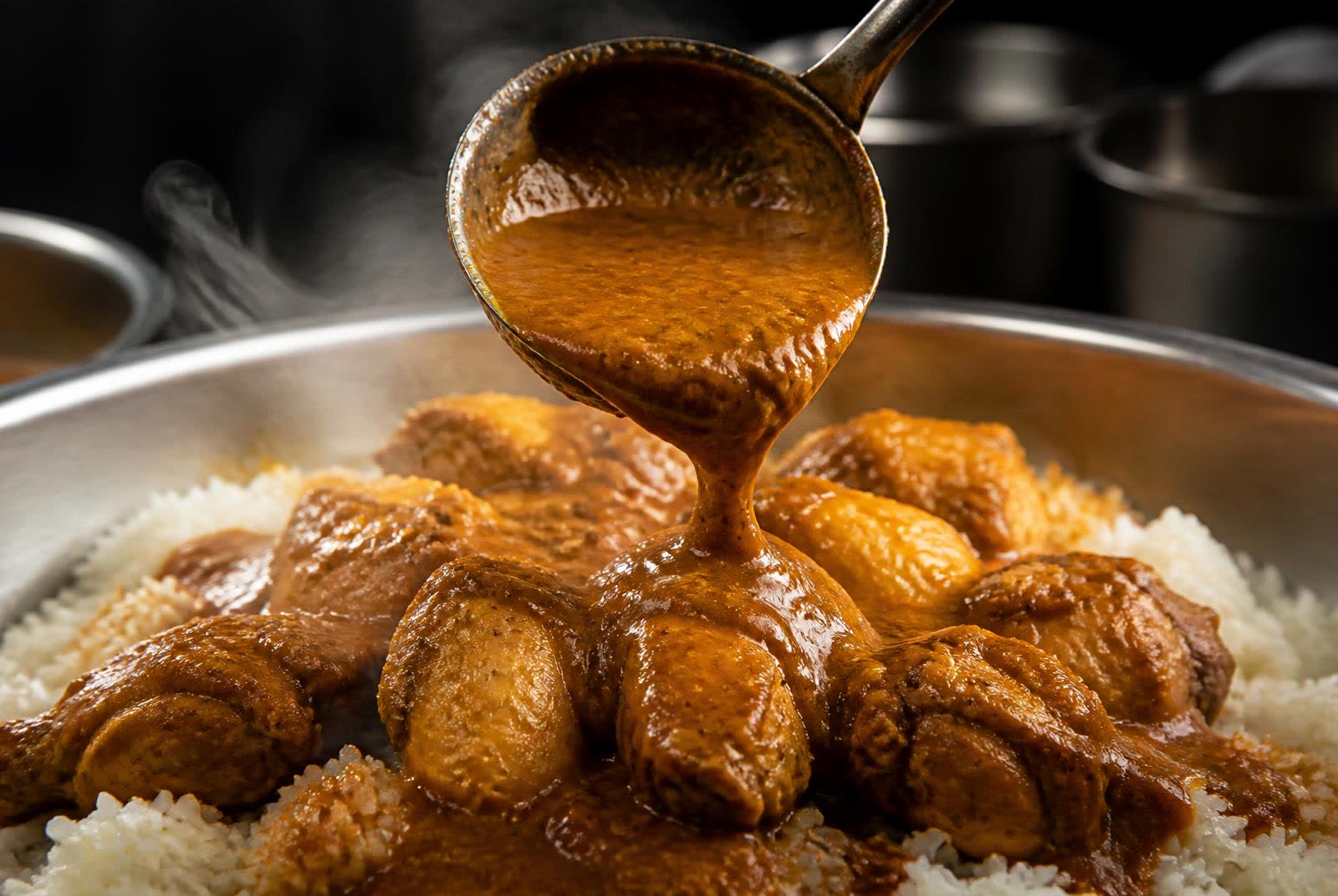 Rich curry sauce ladled over cooked protein and rice in a commercial kitchen pan
